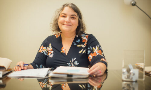 Kathleen at her desk with a stack of paperwork.